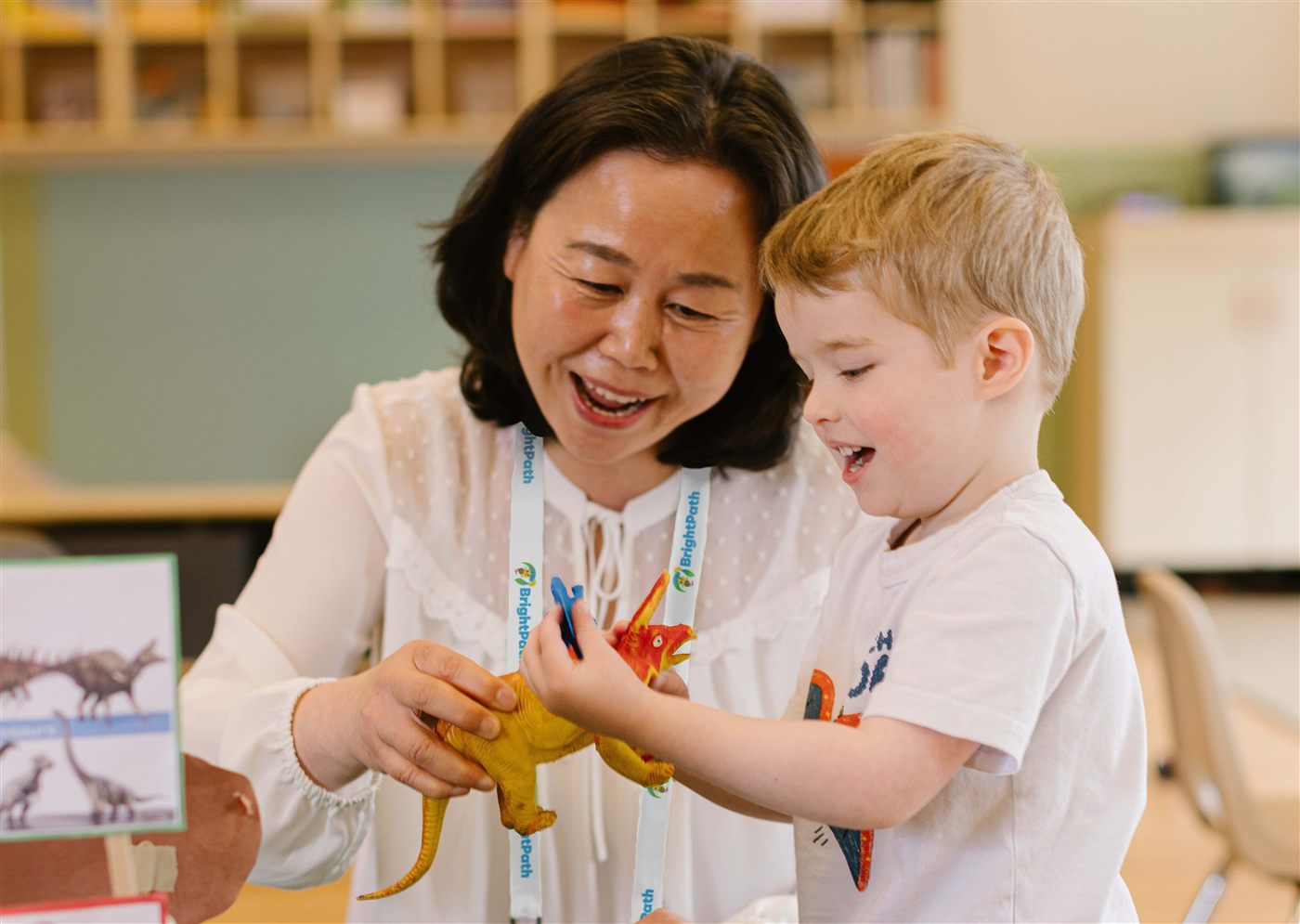 Educator engaging a young child with a toy dinosaur during an inclusive learning activity